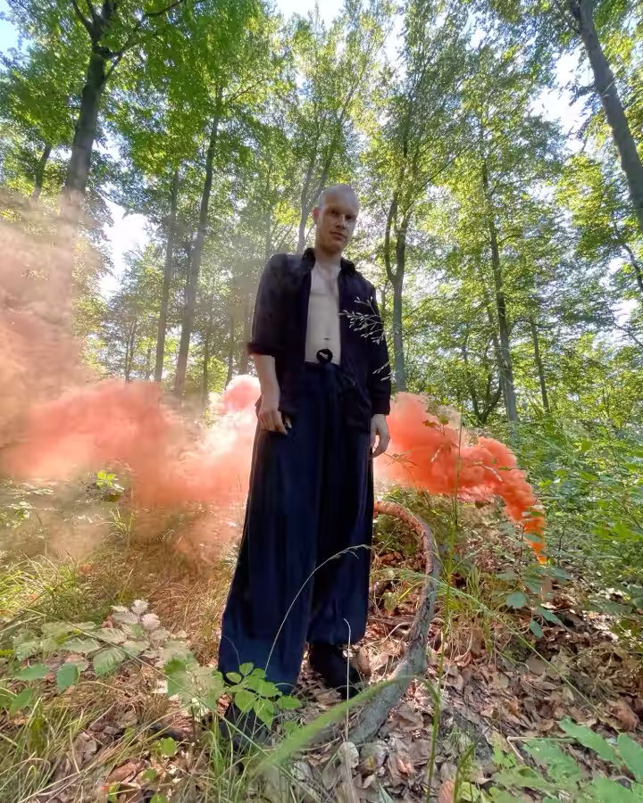 Mr Harry standing in a forest as orange smoke drifts through the trees